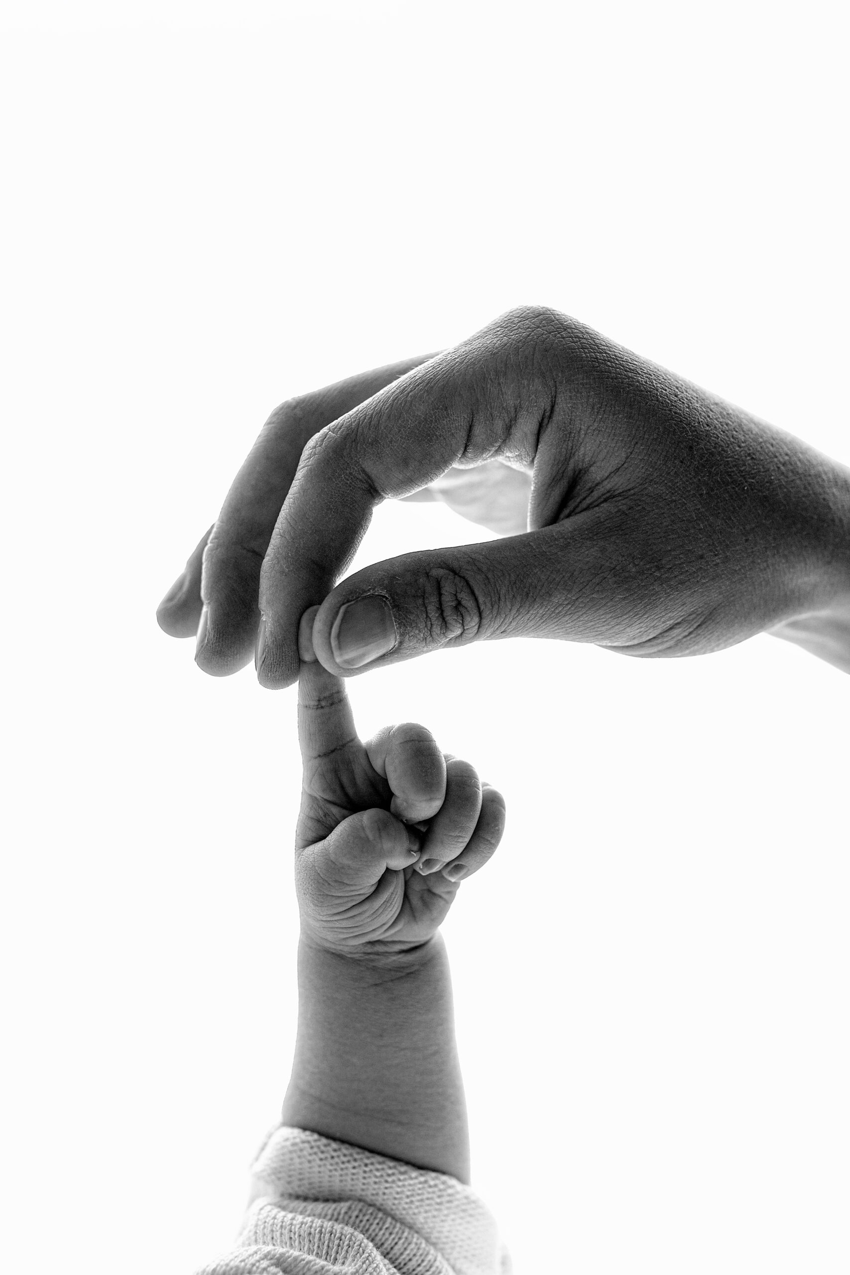 Moeder houdt de vinger van haar pasgeboren baby vast. De foto is in zwart-wit en heeft een witte achtergrond.